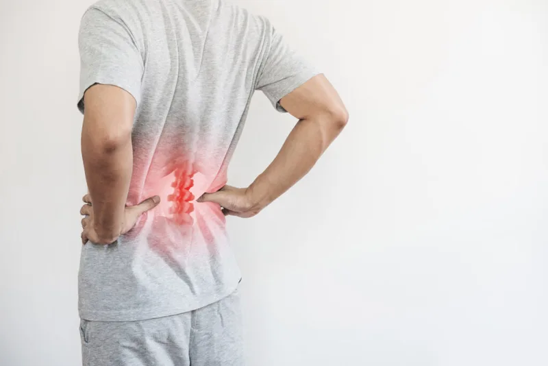Person holding their lower back, with an illustration showing the lumbar spine